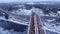 Aerial view tracking from a drone behind a railway train moving on a bridge over a freezing river.