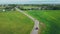 Aerial View Of Tractor Goes On Country Road To Village. Summer Fields Landscape. Top View Of Tractor In Motion On