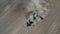 Aerial view of tractor sows seeds in dry ground in field leaving behind cloud of dust.