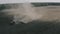 Aerial view of tractor sows seeds in dry ground in field leaving behind cloud of dust.