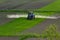 Aerial view of tractor spraying crop in green farm fields with pesticide