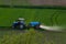 Aerial view of tractor spraying crop in green farm fields with pesticide
