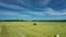 Aerial view of tractor uses trailed bale machine to collect straw in field and make round large bales. Haymaking