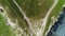 Aerial view of triangle shaped plateau covered with green grass and white paths above the the meadow in sunny summer day