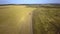 Aerial view of a truck driving on dirt road between plowed fields making lot of dust.