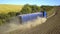 Aerial view of a truck driving on dirt road between plowed fields making lot of dust.