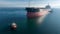 Aerial view of tug boat assisting big cargo ship. Large cargo ship enters the port escorted by tugboats