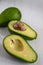 Aerial view of two half avocados with seed and whole avocado on white wood, vertical