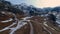 Aerial view of a very slow downward movement over a road in a valley with snow and high mountains in front of us