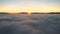 Aerial view of vibrant sunset over white dense clouds with distant dark mountains on horizon.