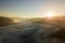 Aerial view of vibrant sunset over white dense foggy clouds with distant dark silhouettes of mountains on horizon