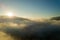 Aerial view of vibrant sunset over white dense foggy clouds with distant dark silhouettes of mountains on horizon