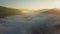 Aerial view of vibrant sunset over white dense foggy clouds with distant dark silhouettes of mountains on horizon.