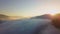 Aerial view of vibrant sunset over white dense foggy clouds with distant dark silhouettes of mountains on horizon.