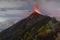Aerial view of Volcano de Fuego, erupting, covered with trees, with smoke and lava around the top