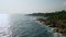 Aerial view of waves hitting rocky shore near hilltop lighthouse. Scenic coastline panorama for mariners, tourists