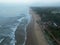 Aerial view of the wavy seacoast and dense foggy forest with several buildings under the foggy sky