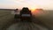 Aerial view of wheat three silhouette of harvests works in field with sunset on background.