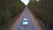 Aerial view white business car starts moving on village road among summer forest at evening