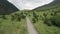 Aerial view of a white car moving on mountain rural road along wilderness. Action. Car driving on straight road during