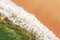 aerial view of white waves from an emerald green ocean crashing onto a sandy beach