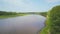 Aerial view of a wide river among green trees, smooth bend of channel. Clip. Forest on the shore of reservoir, summer