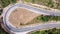 Aerial view of winding road in high mountain pass trough green pine woods.