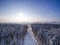 Aerial view on winter forest and field. Sunny day in snowfall, snowflakes on sunlights. Lake and river on background. Country road