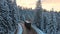 Aerial view of winter landscape with snow covered mountain hills and winding forest road with driving vehicles in morning.