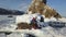 Aerial view of a woman playing steel tongue drum while sitting on a rock among snow and ice of a frozen lake. Clip