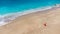 Aerial view of woman in red dress sitting on the sandy beach with a baby, enjoying soft turquoise ocean wave. Tropical sea in