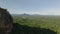 Aerial view of wooded landscape on sunny day. Backwards reveal of rock wall with stairs for tourists. Sigiriya, Sri