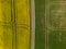 aerial view of a yellow rapeseed field and green wheat field divided by a rustic dirt road.