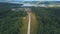 Aerial village road through the forest and the fields. Clip. Road leading through forest in village. Aerial view