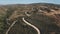 Aerial winding road among trees along sandy hills. Blue sky over mountain range. Traveling hiking