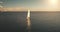 Aerial of yacht cruising in ocean waters at sun. White sail boat at open sea. Serene seascape