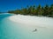 AERIAL: Young woman relaxing in the glassy ocean water by the lush exotic island