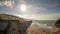 Aerical shot of a beach beside a mountain cliff with the bright sun in the sky