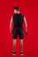 Aerobic workout. Back view of strong young man standing with skipping rope on red studio background