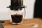 Aeropress and glass cup, spoon on wooden table, coffee drops closeup in glass. Professional barista preparing coffee alternative