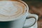 Aesthetic closeup of latte art in a white coffee mug on a blurred wooden surface