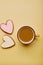 Aesthetics coffee cup and cookies in shape of heart. Spring card with baked glazed cookies on yellow background