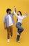 Affectionate indian couple holding hands and dancing together over yellow background, enjoying favourite song, crop