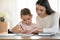 Affectionate young mother teaching small daughter reading writing.