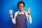 African american barista woman wearing bartender uniform holding cup over blue background doing ok sign with fingers, excellent