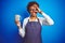 African american barista woman wearing bartender uniform holding cup over blue background with happy face smiling doing ok sign