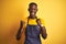 African american bartender man wearing apron standing over isolated yellow background celebrating surprised and amazed for success