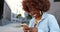 African American beautiful woman tapping and scrolling on mobile phone and laughing outdoor. Stylish attractive female