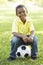 African American Boy Sitting On Football In Park