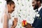 African american bride looking at present near happy bridegroom and flowers